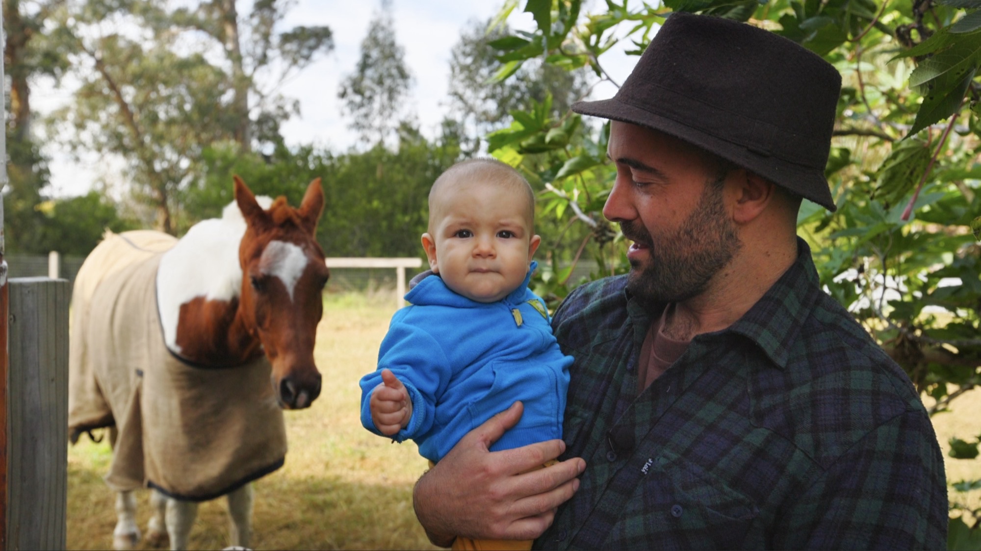 Martín holding his baby son, with Fidei, a tobiano paint horse, behind them
